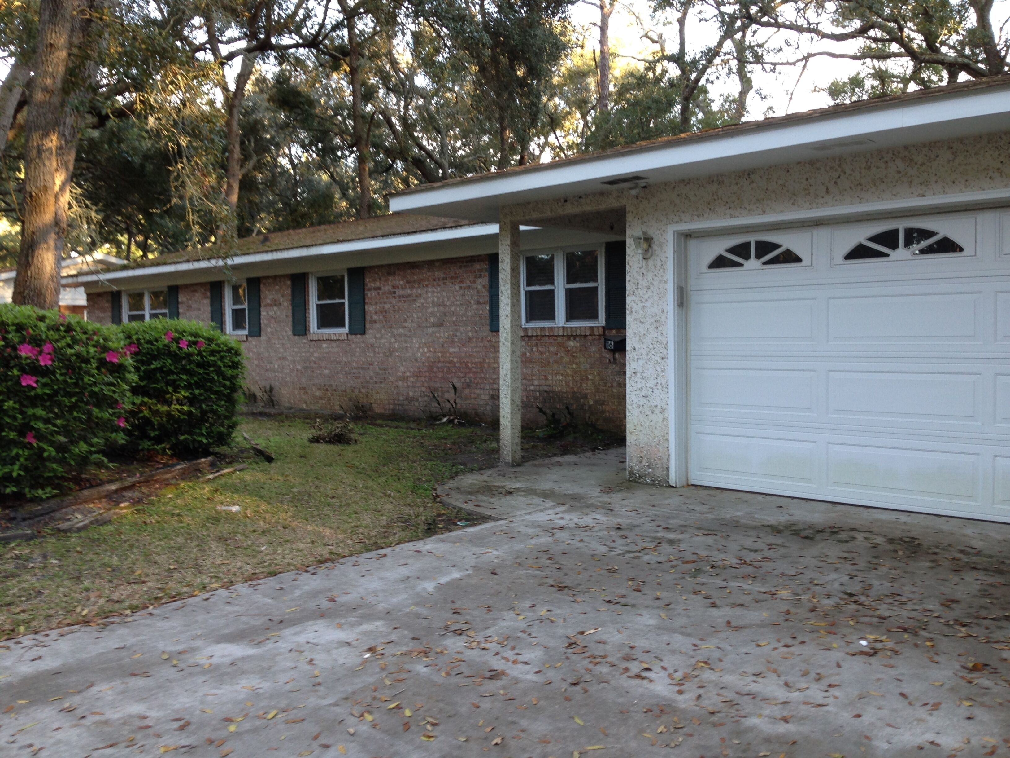 A single-story house with a garage, a covered porch, and a small front yard with grass and a few trees.