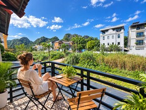 Uma pessoa sentada à mesa de madeira numa varanda, com vista para uma área residencial e colinas.