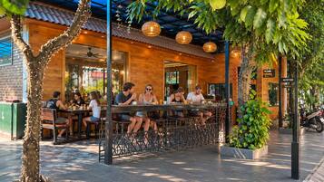 An outdoor seating area with tables and chairs, surrounded by greenery and a building with a wooden facade.