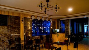 A restaurant with brick walls, wooden paneling, and a large window with a city view. There are multiple tables and chairs arranged for dining. - Tam Coc Mandala Villa & Homestay  (Nam Hoa Lu)
