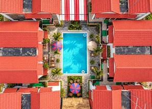Una piscina en la azotea rodeada de edificios con tejados rojos, con mesas y sillas al aire libre y sombrillas.
