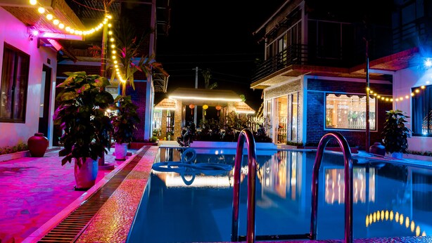 A nighttime pool area with string lights, a clear pool, and potted plants. - Tam Coc Mandala Villa & Homestay  (Nam Hoa Lu)