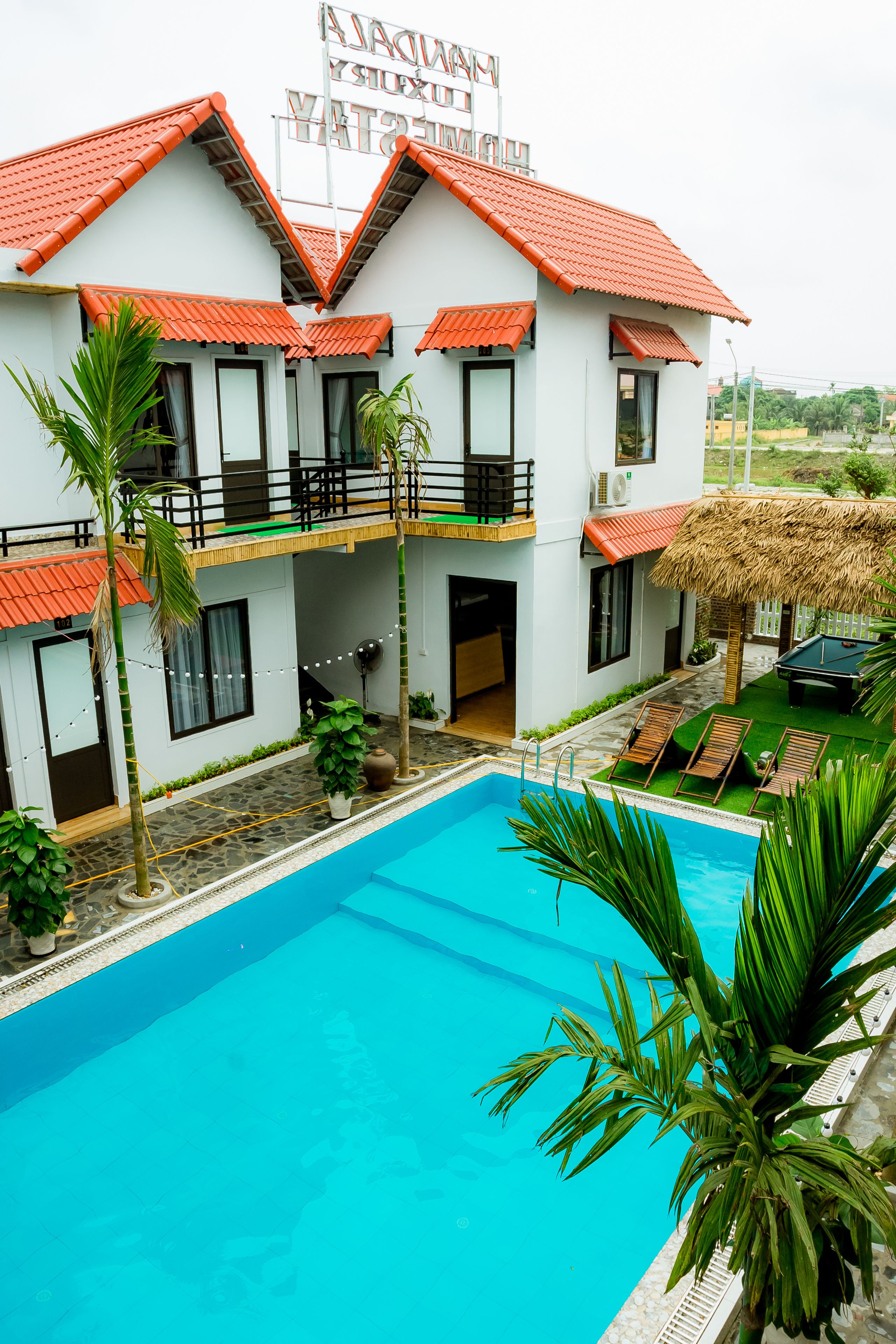 A two-story building with a swimming pool, a thatched roof, and a sign indicating it is a hotel.