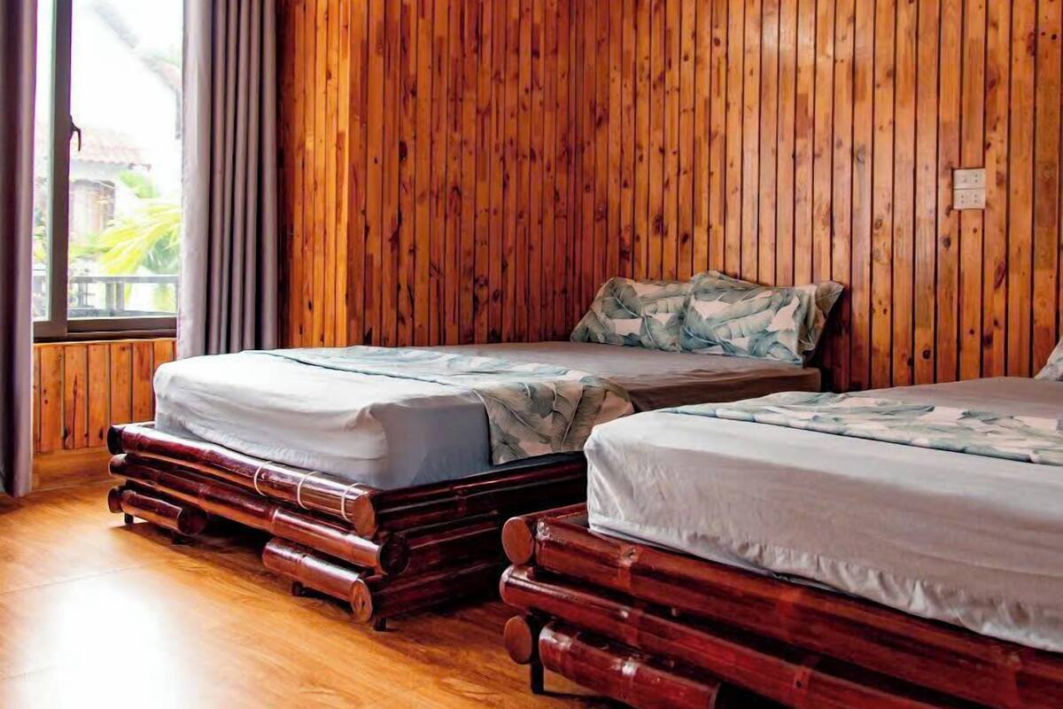 A room with wooden panel walls, two beds with mattresses, a window with curtains, and a wooden floor.