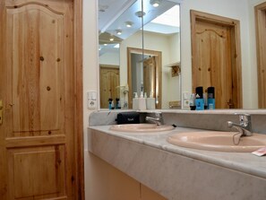 Une salle de bain avec des portes en bois, deux lavabos, un grand miroir et des articles de toilette posés sur le comptoir.