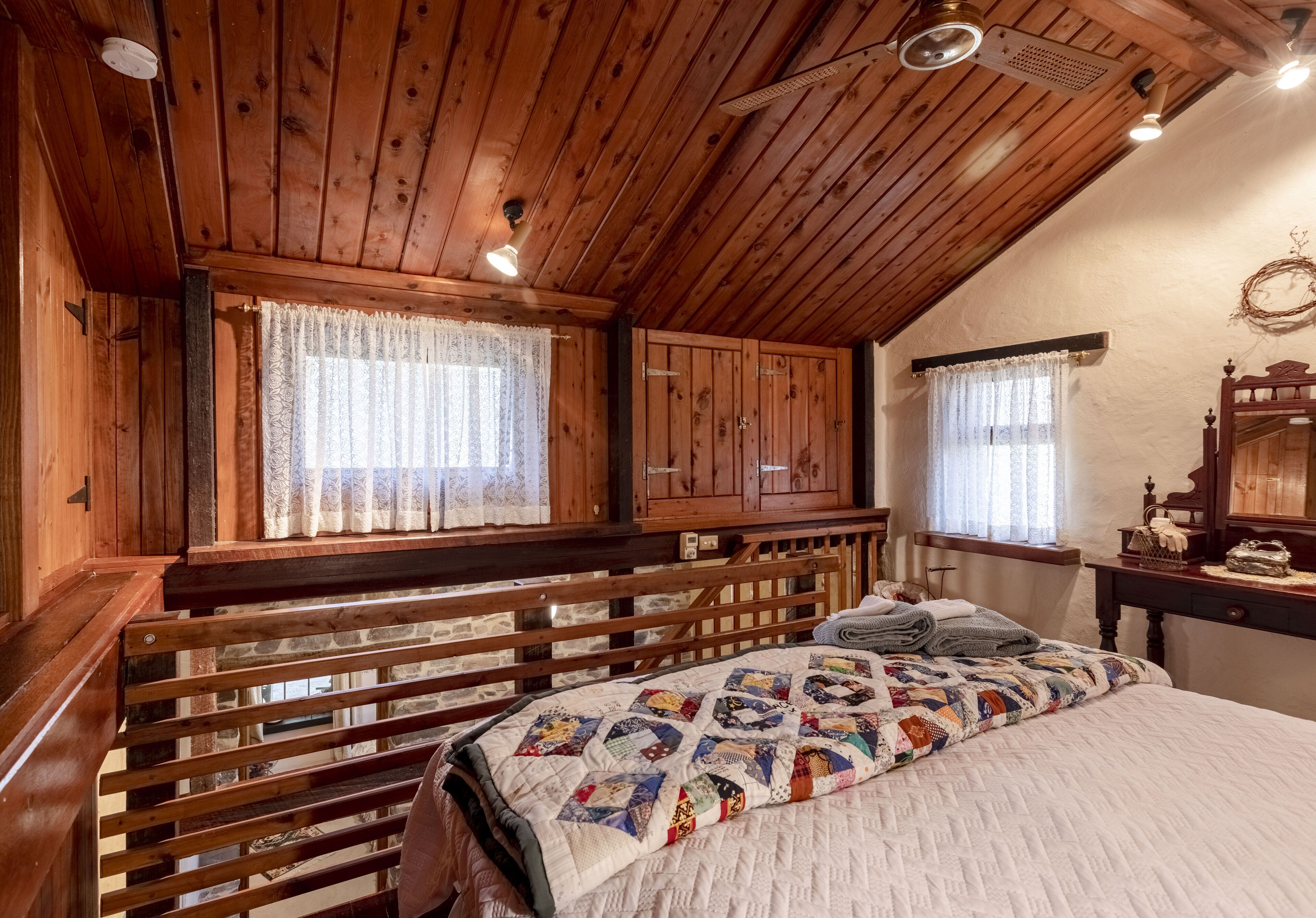 Ein Schlafzimmer einer Holzhütte mit Bett, zwei Vorhängen und einem Holz-Kopfteil, sowie einem Deckenventilator.