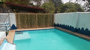 A swimming pool with clear blue water, surrounded by a bamboo fence, and a tiled edge.