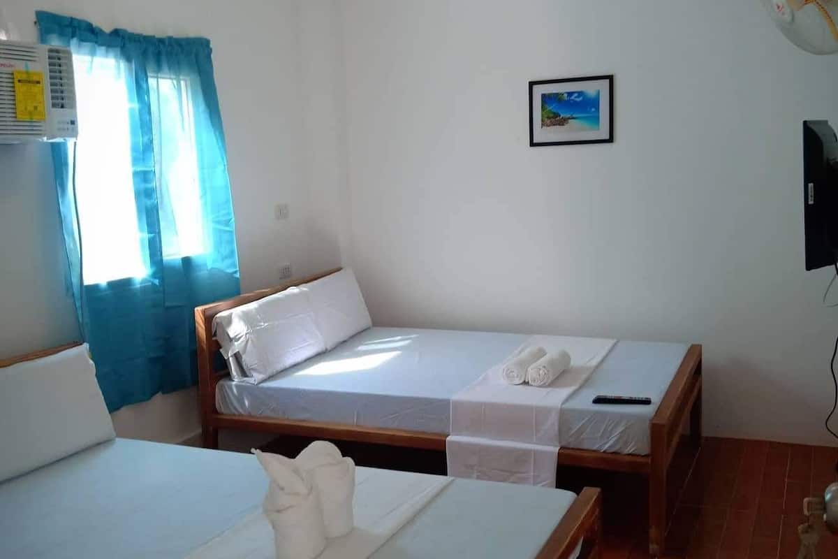 A room with two wooden beds, a ceiling fan, a wall-mounted TV, and a window with blue curtains.