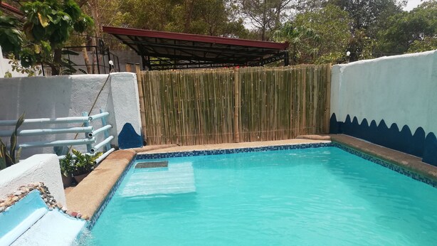 A swimming pool with a tiled edge, surrounded by a bamboo fence and a white wall with a blue decorative border.