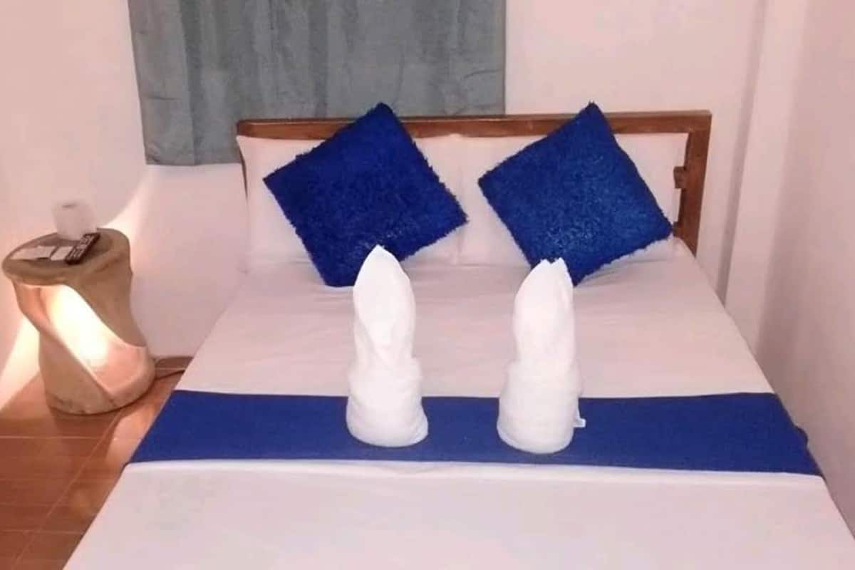 A bed with a blue bedspread and two white towels arranged to resemble a pair of legs.