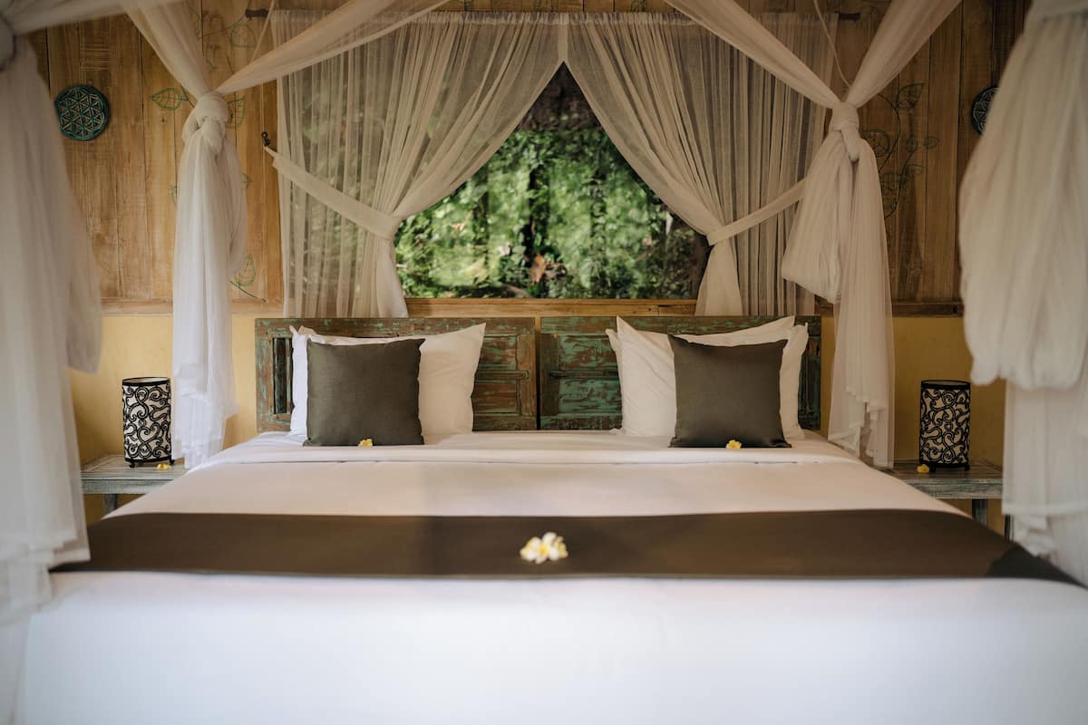 Cama com dossel, cabeceira de madeira e vista para o verde lá fora.