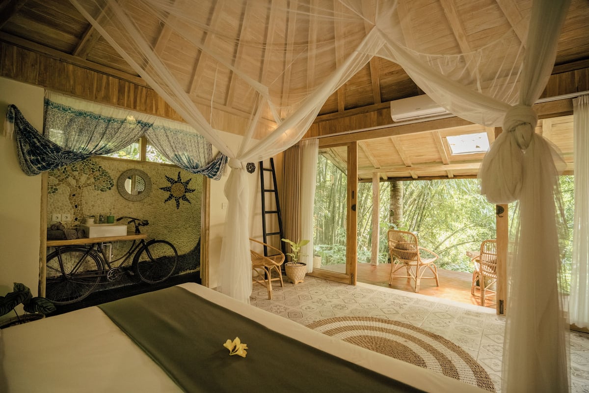 Quarto com cama, bicicleta, escada e vista para o exterior.