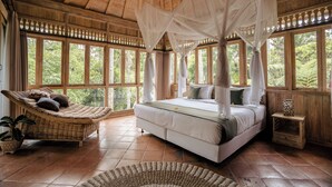 A spacious bedroom with a large bed, a hanging chair, and a small bedside table. - Basundari Retreat Bali (Ubud)