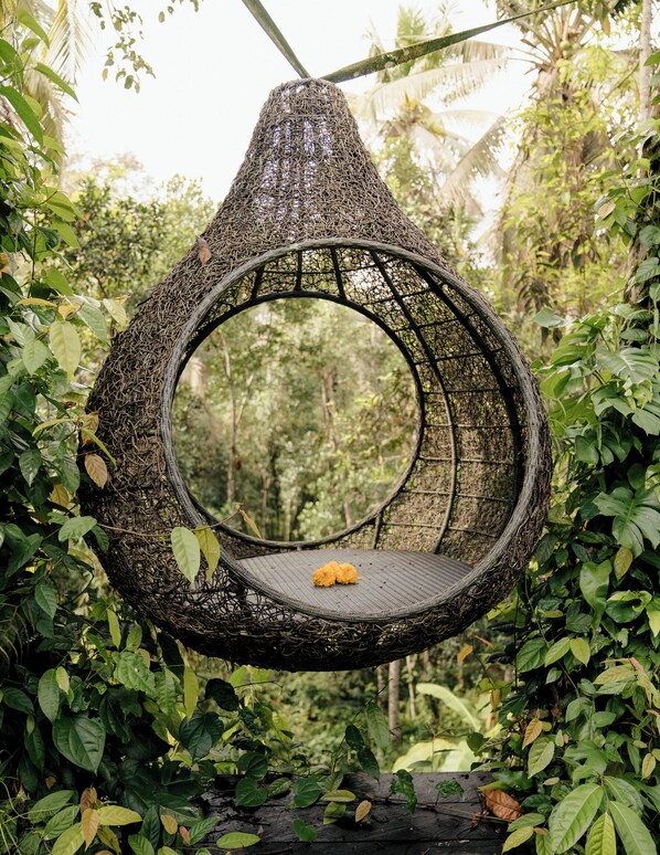 A circular wicker swing chair suspended by a rope, surrounded by dense foliage. - Basundari Retreat Bali (Ubud)