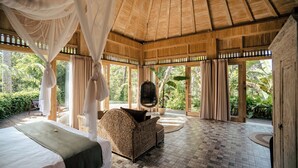 A room with a bed, a wicker sofa, a hanging chair, and a large window with curtains. - Basundari Retreat Bali (Ubud)