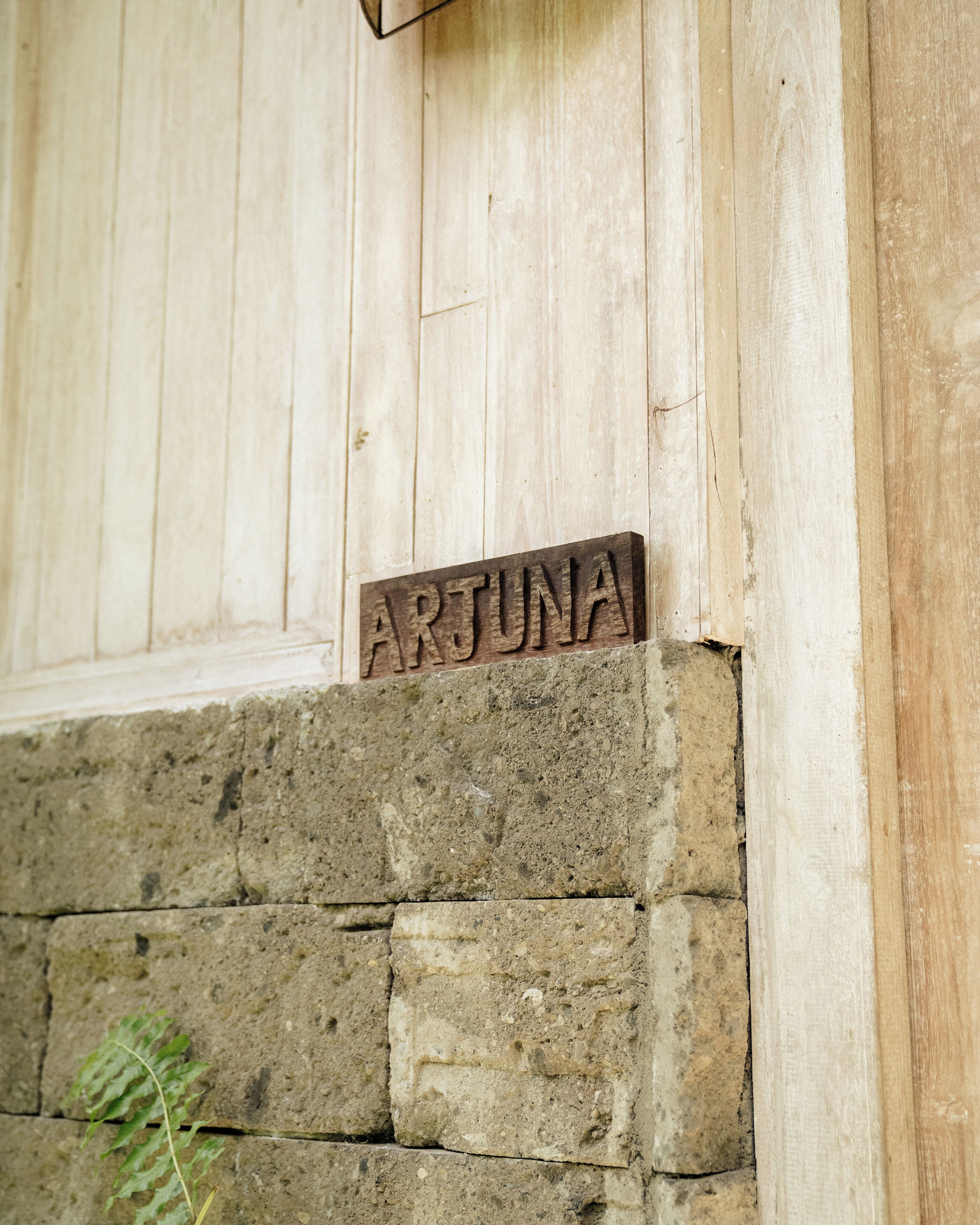 A wooden sign with the name 'ARTUNA' mounted on a stone wall.
