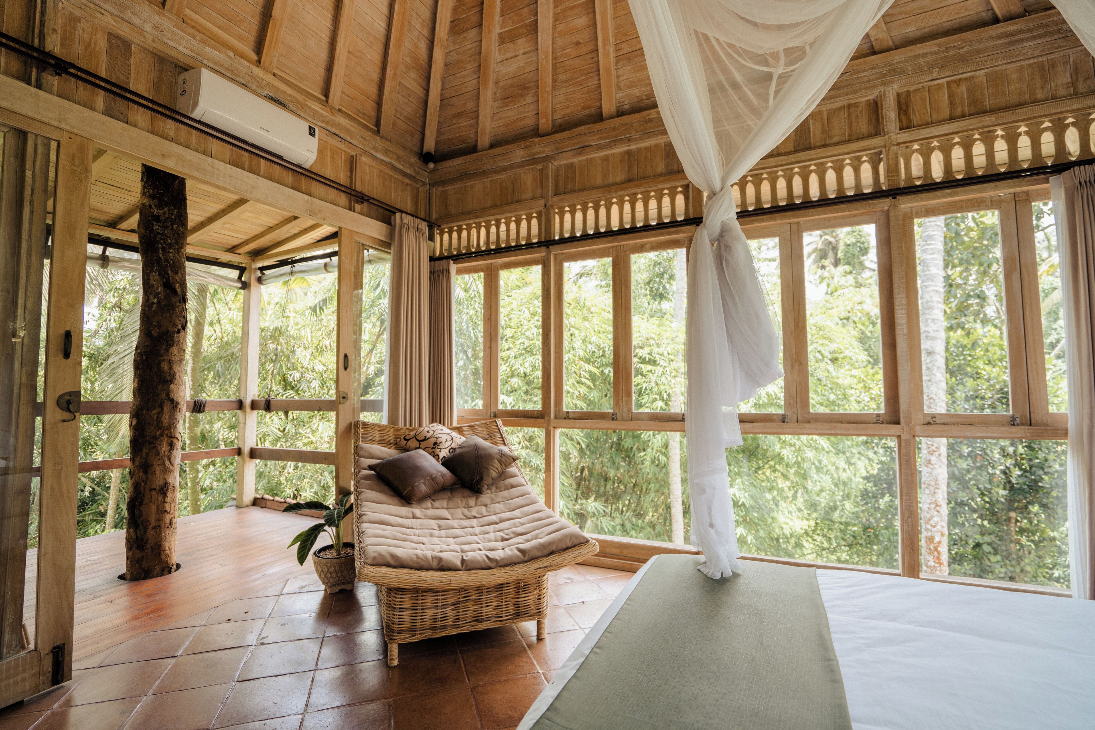 A room with a large window, a bed, a wicker chair, and a ceiling fan.