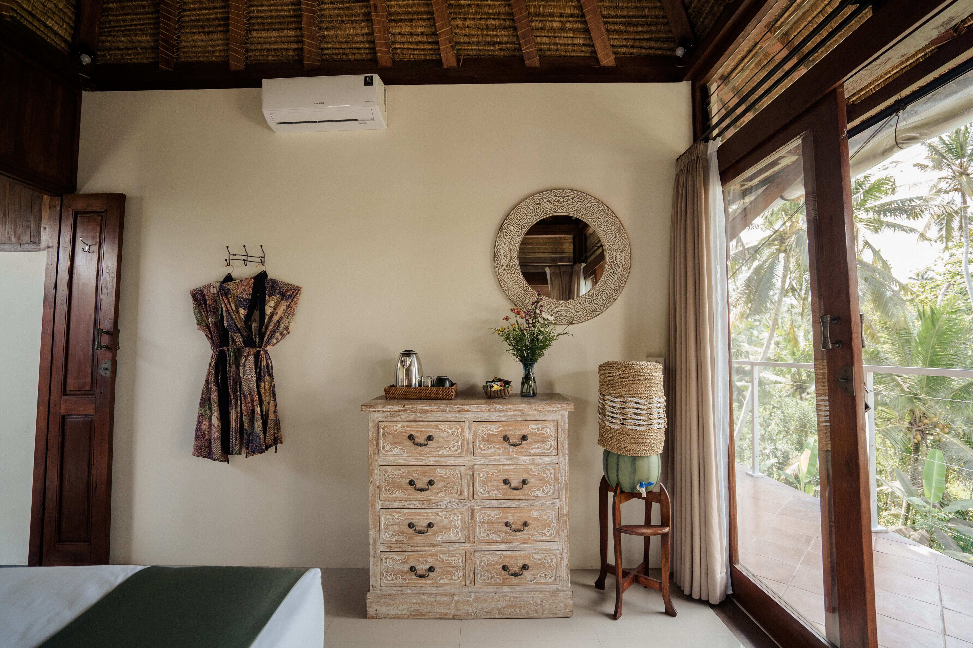 A room with a wooden dresser, a mirror, and a view of palm trees.