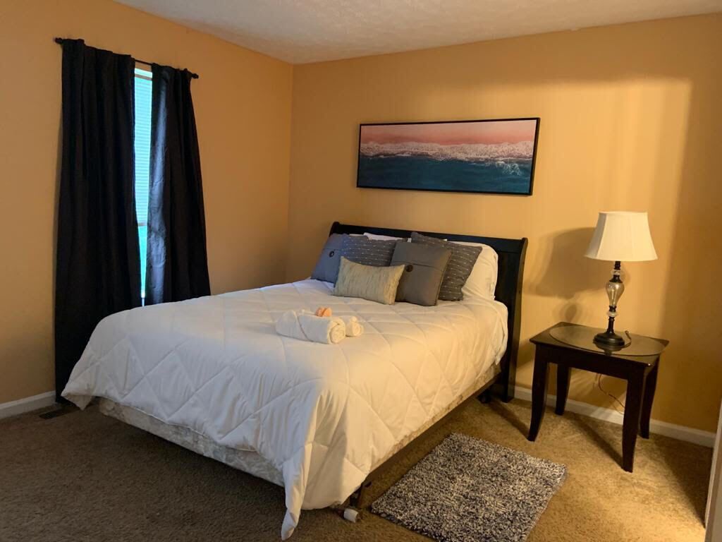 A neatly made bed with pillows, a bedside table with a lamp, and a painting on the wall.