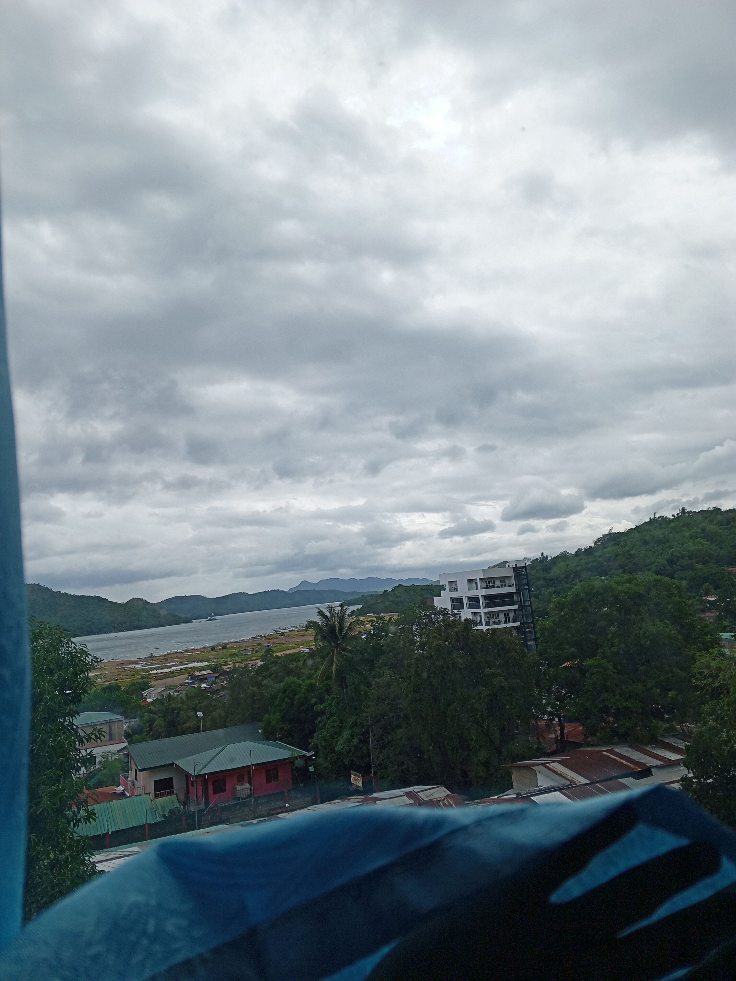 A view of a coastal area with a building on a hill, a body of water, and greenery.