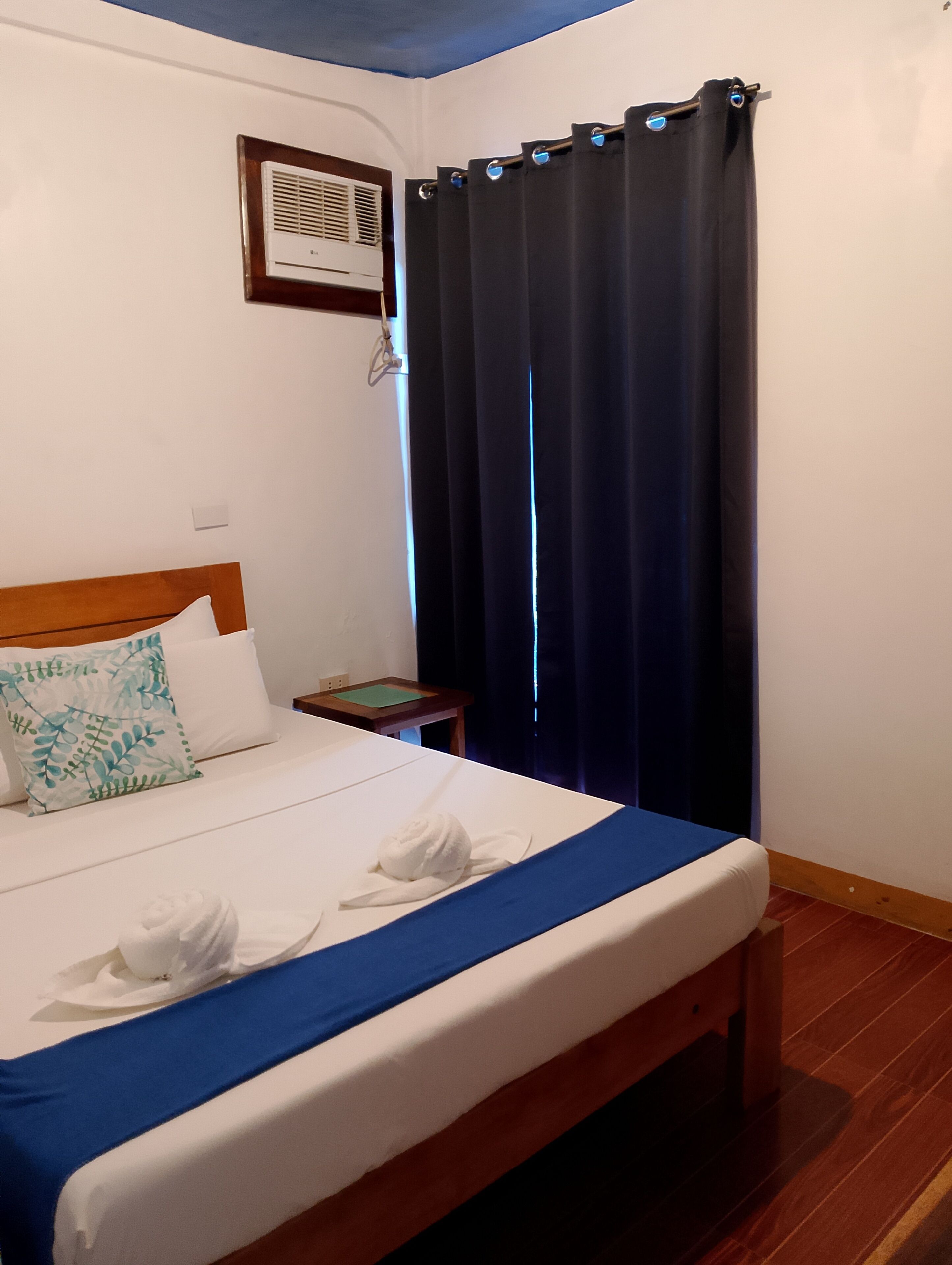 A hotel room with a bed, a nightstand, a wall-mounted air conditioner, and a window with curtains.