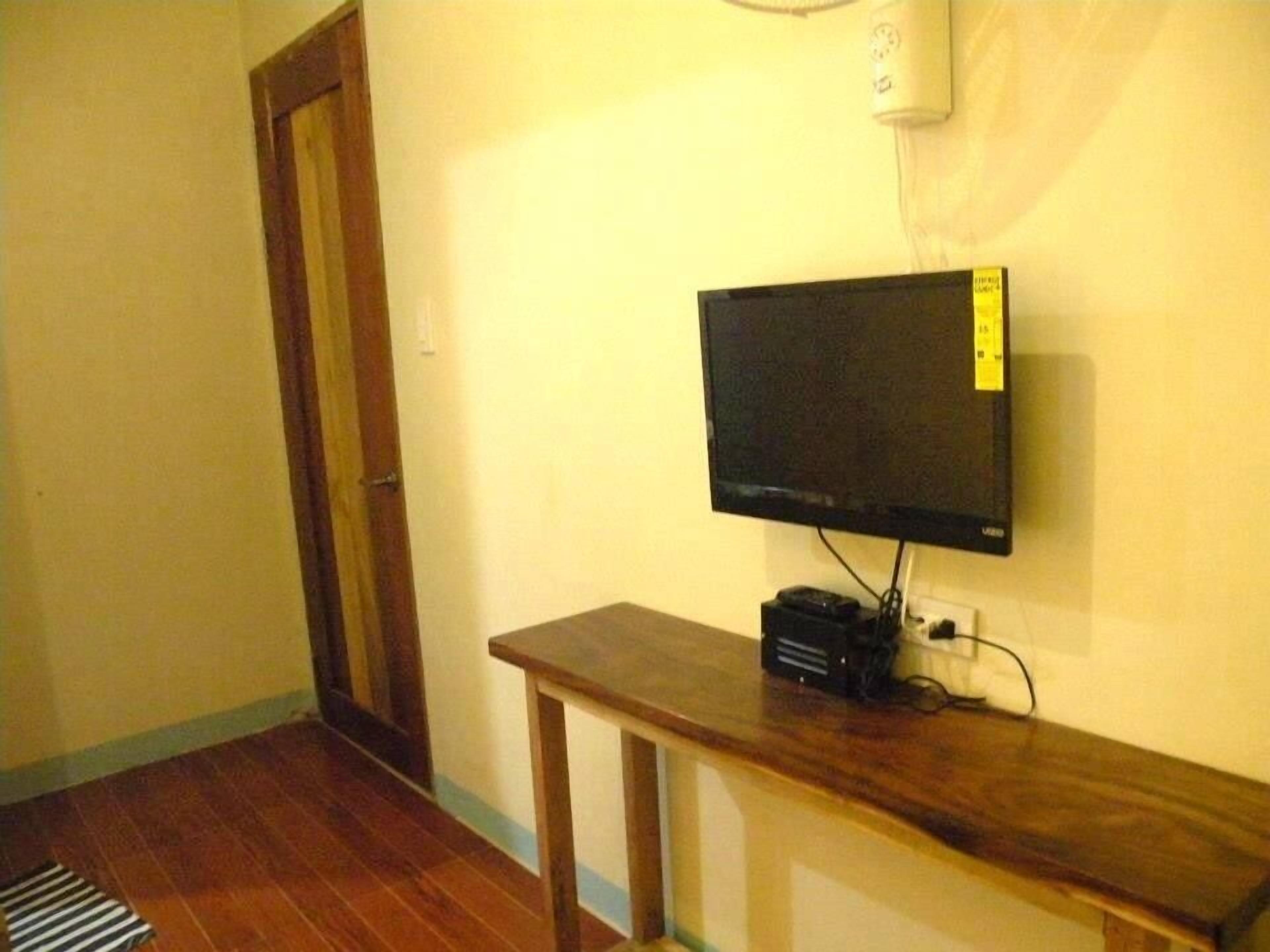 A room with a wooden floor, a television on a stand, a door, and a wall-mounted air conditioner.