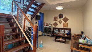 A spacious living area with a wooden staircase, a sofa set, a coffee table, and a wall decorated with geometric patterns. - Casa Montemar B&B (Coron)