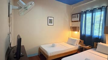 A bedroom with two beds, a desk with a computer, a wall-mounted fan, and an air conditioning unit.