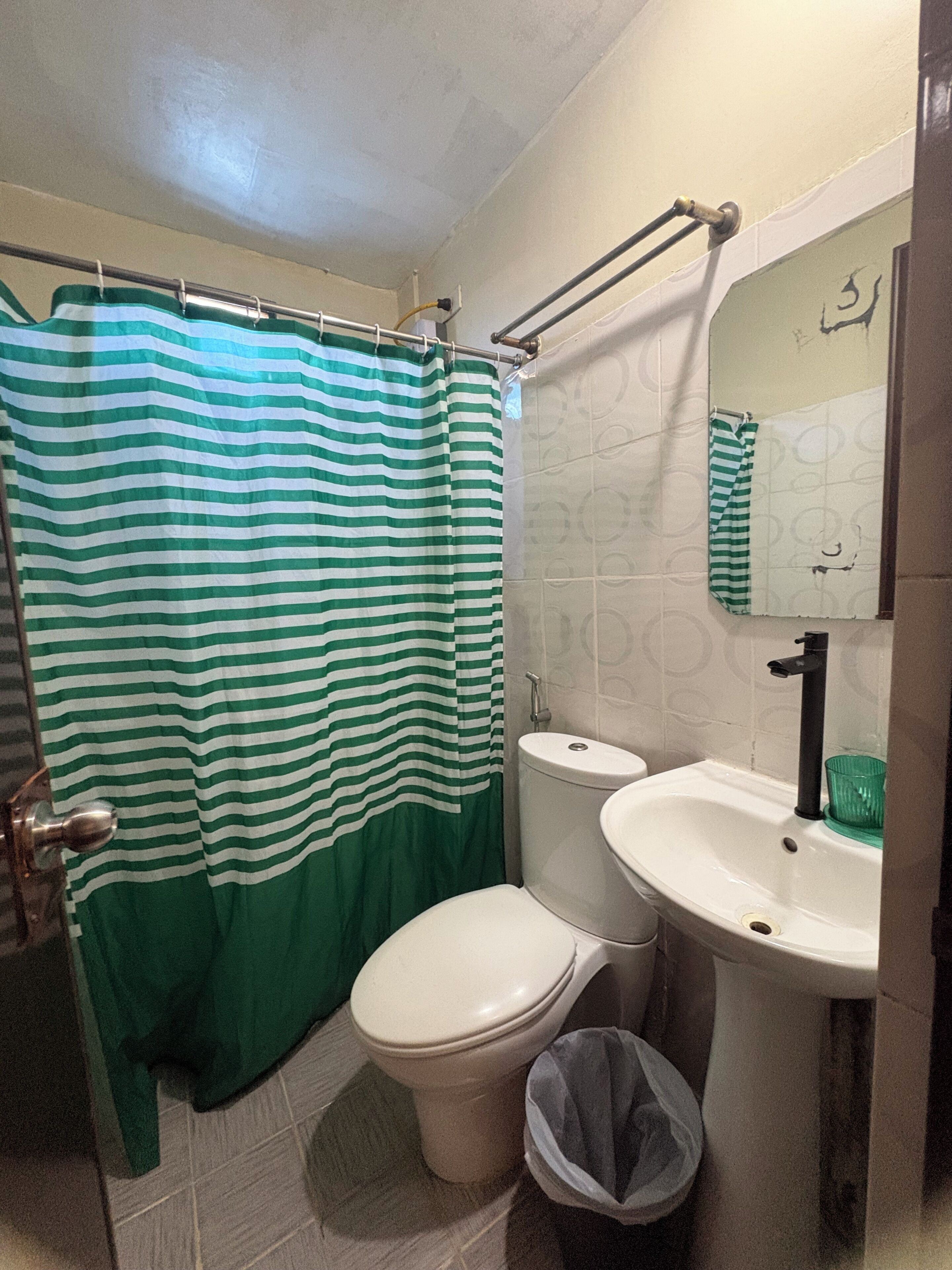 A bathroom with a striped shower curtain, a toilet, a sink, and a trash bin.