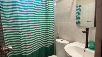 A bathroom with a striped shower curtain, a toilet, a sink, and a trash bin.