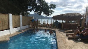 A swimming pool with clear blue water, surrounded by lounge chairs and umbrellas, with a view of mountains in the background. - Casa Montemar B&B (Coron)