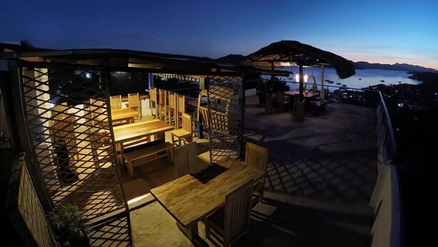 An outdoor seating area with wooden furniture and a view of the sea at dusk. - Casa Montemar B&B (Coron)