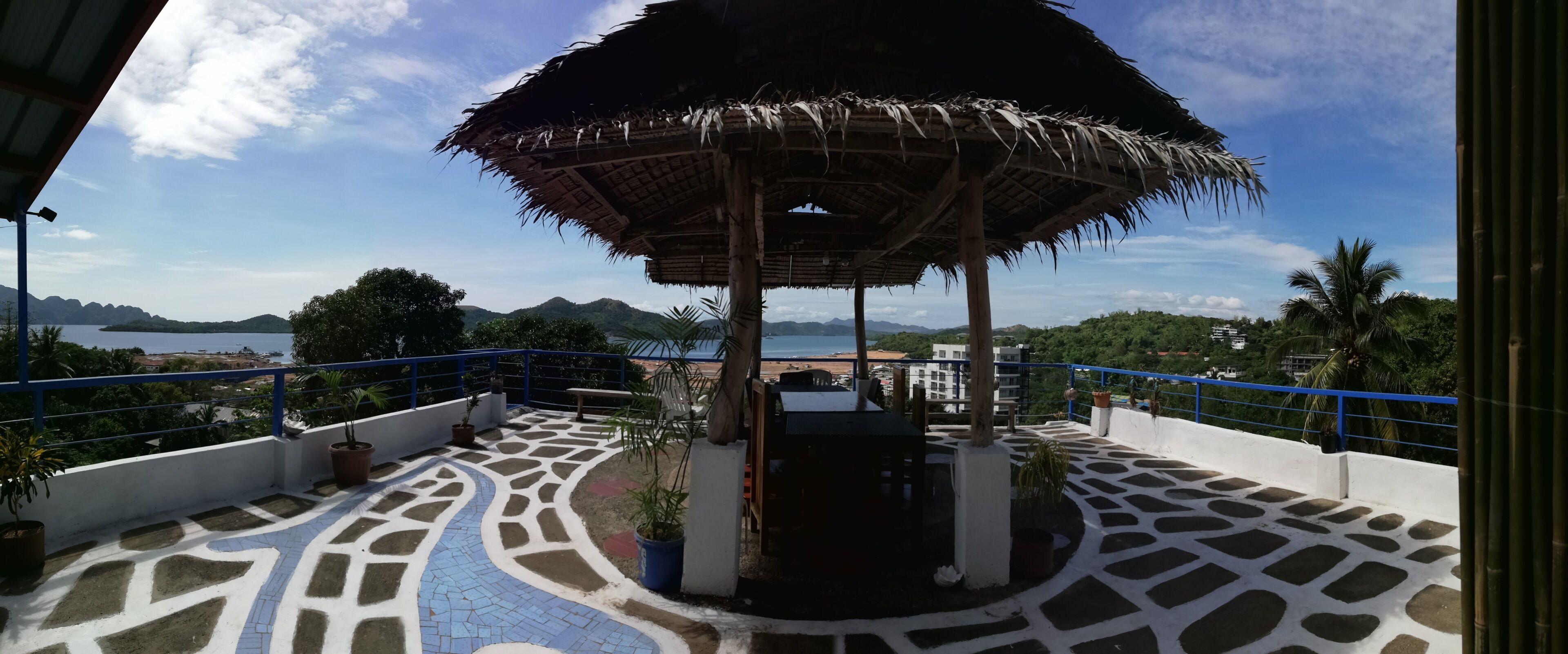 Une terrasse sur le toit agrémentée d’un gazebo à toit de chaume, de plantes en pot et d’un sol à motifs.