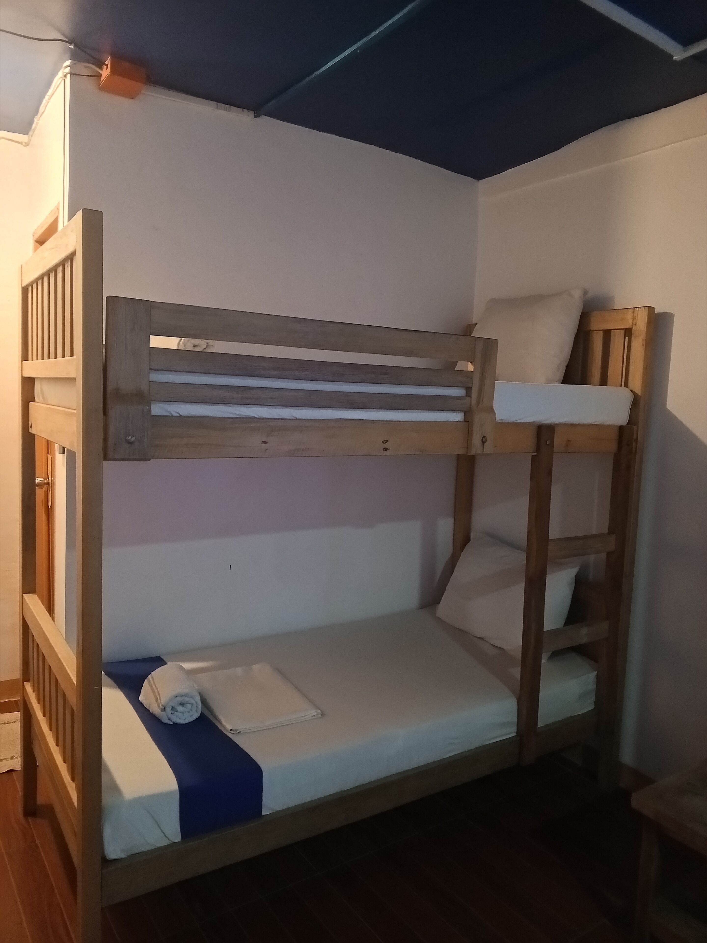 Una cama litera con estructura de madera, un colchón, almohadas y una toalla enrollada.