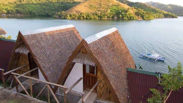 Thatched-roof huts with a view of a calm lake and hills in the background.