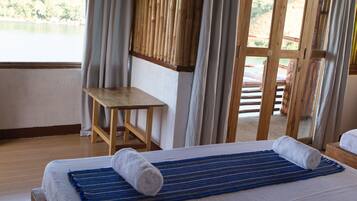 A hotel room with a bed, a wooden table, and a view of a lake through a large window.