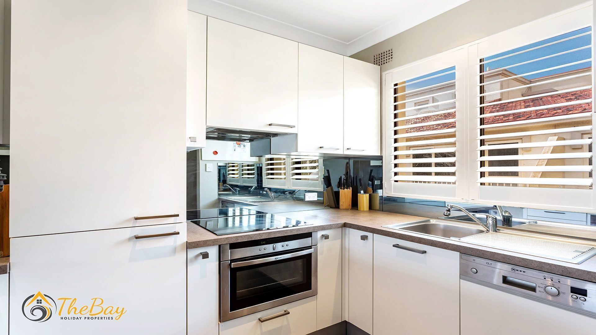 A modern kitchen with white cabinetry, stainless steel appliances, and a window with blinds.