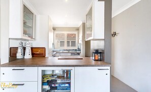 Una cocina con lavavajillas integrado, una ventana con persianas y un refrigerador pequeño.