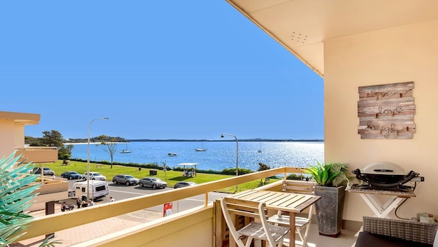 En balkong med utsikt över havet, en grill och ett matbord.