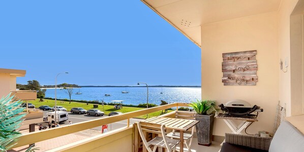 Un balcón con vista al mar, una parrilla y una mesa de comedor.