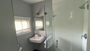 A modern bathroom with a glass shower enclosure, a white sink, and a toilet. - Crocker Inn (Vineyard Haven)