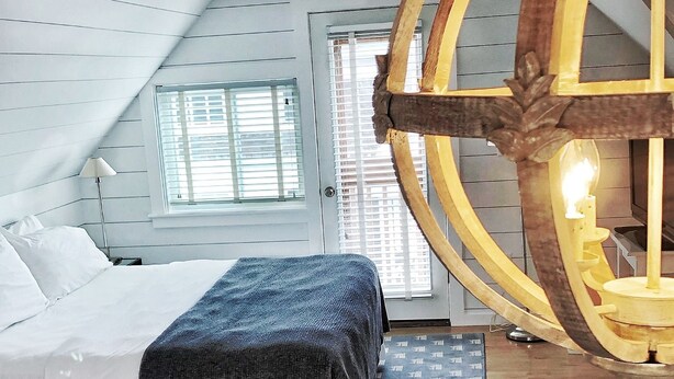 A bedroom with a sloped ceiling, a bed with white linens, a blue patterned rug, and a wooden floor. - Crocker Inn (Vineyard Haven)