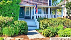A two-story house with a front porch, a flag, and a brick pathway leading to the entrance. - Crocker Inn (Vineyard Haven)