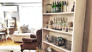 A cozy living room with a wooden floor, a white sofa, a brown armchair, and a bookshelf filled with bottles and jars. - Crocker Inn (Vineyard Haven)