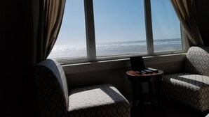 A room with a large window overlooking the ocean, two patterned chairs, and a small table with a laptop and remote controls. - Beach Escape - Waldport (Waldport)