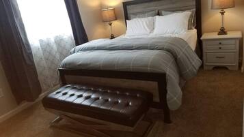 Une chambre à coucher avec un lit, deux tables de chevet avec des lampes, un banc et une fenêtre avec des rideaux.