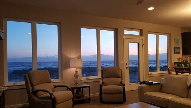 A living room with large windows offering a view of the ocean and mountains. There are two armchairs, a sofa, and a coffee table. - Beach Escape - Waldport (Waldport)