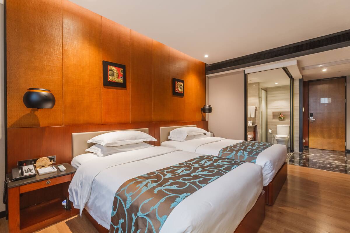A hotel room with two beds, wooden headboards, a nightstand with a phone, and a mirror.
