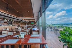 Un restaurant avec des tables et des chaises en bois, un coin bar et une vue sur la ville et les montagnes.