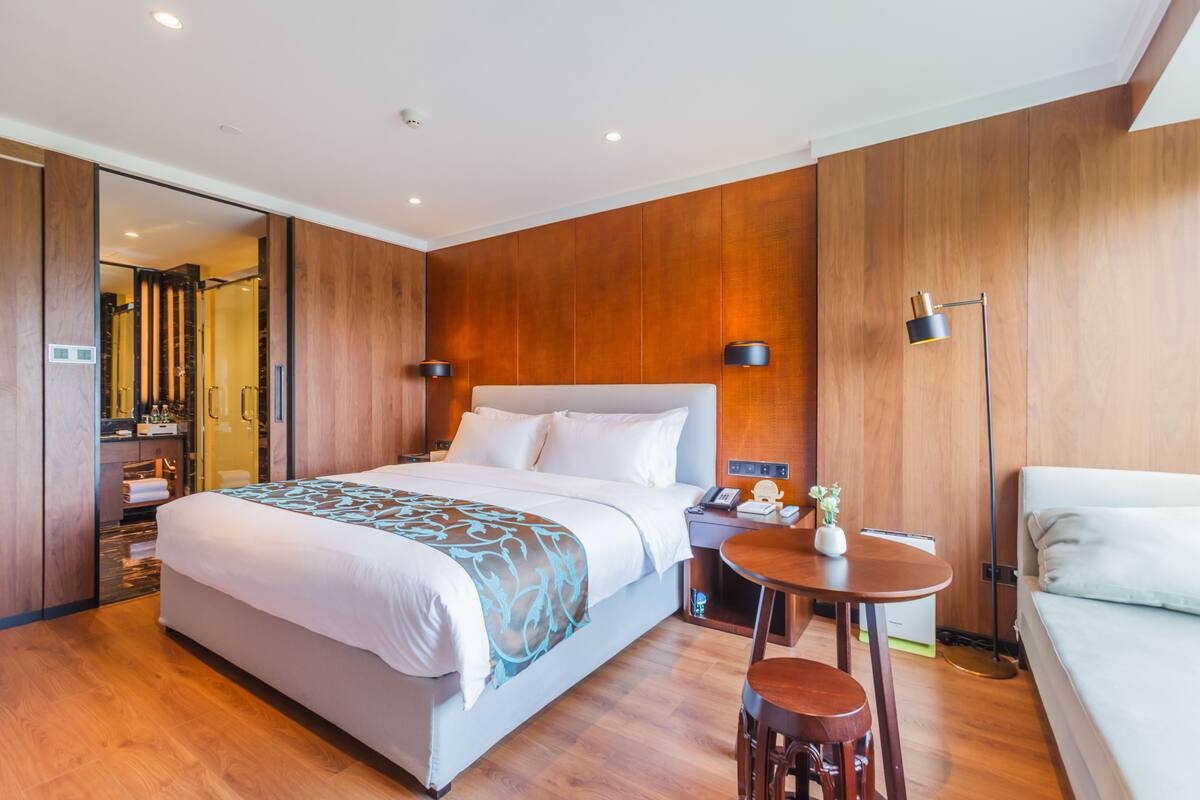 A modern hotel room with a large bed, bedside tables, a small round table, and a sofa.